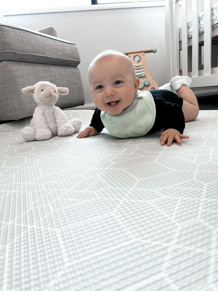 A baby is comfortably positioned on a round mat, engaging with several bright toys nearby.

