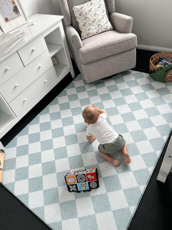  A baby happily plays on a blue and white checkered rug, surrounded by toys and a cheerful atmosphere.