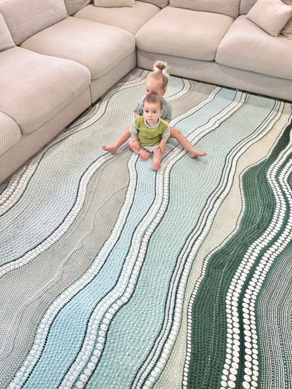A child sits on a rug patterned with waves, smiling and playing with toys around them.