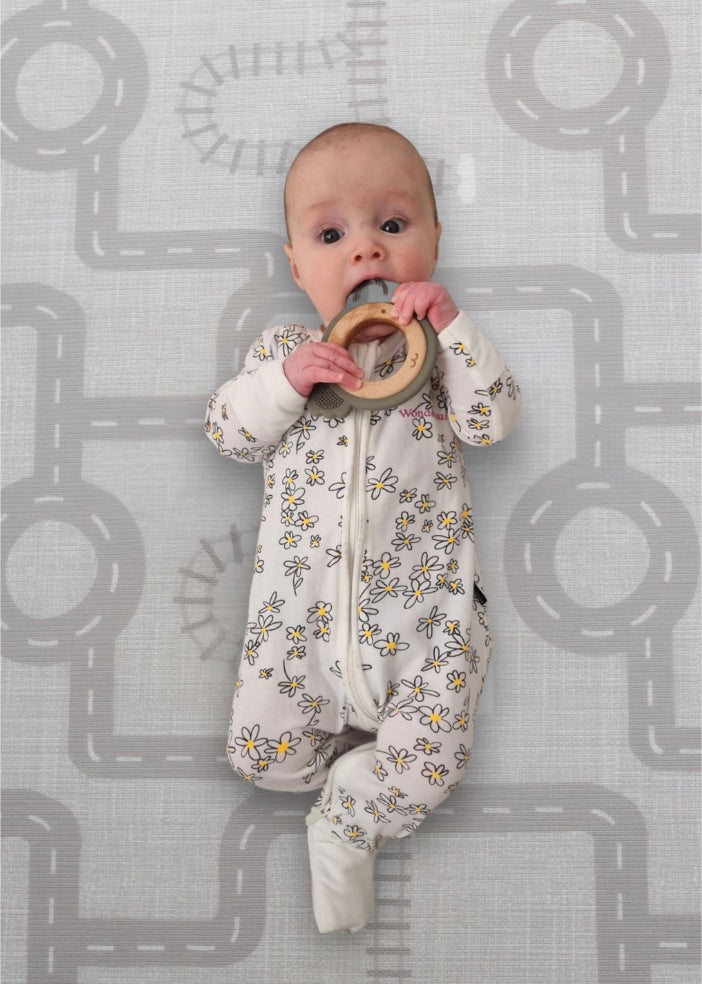 A baby lies on a mat, happily chewing on a colorful toy.